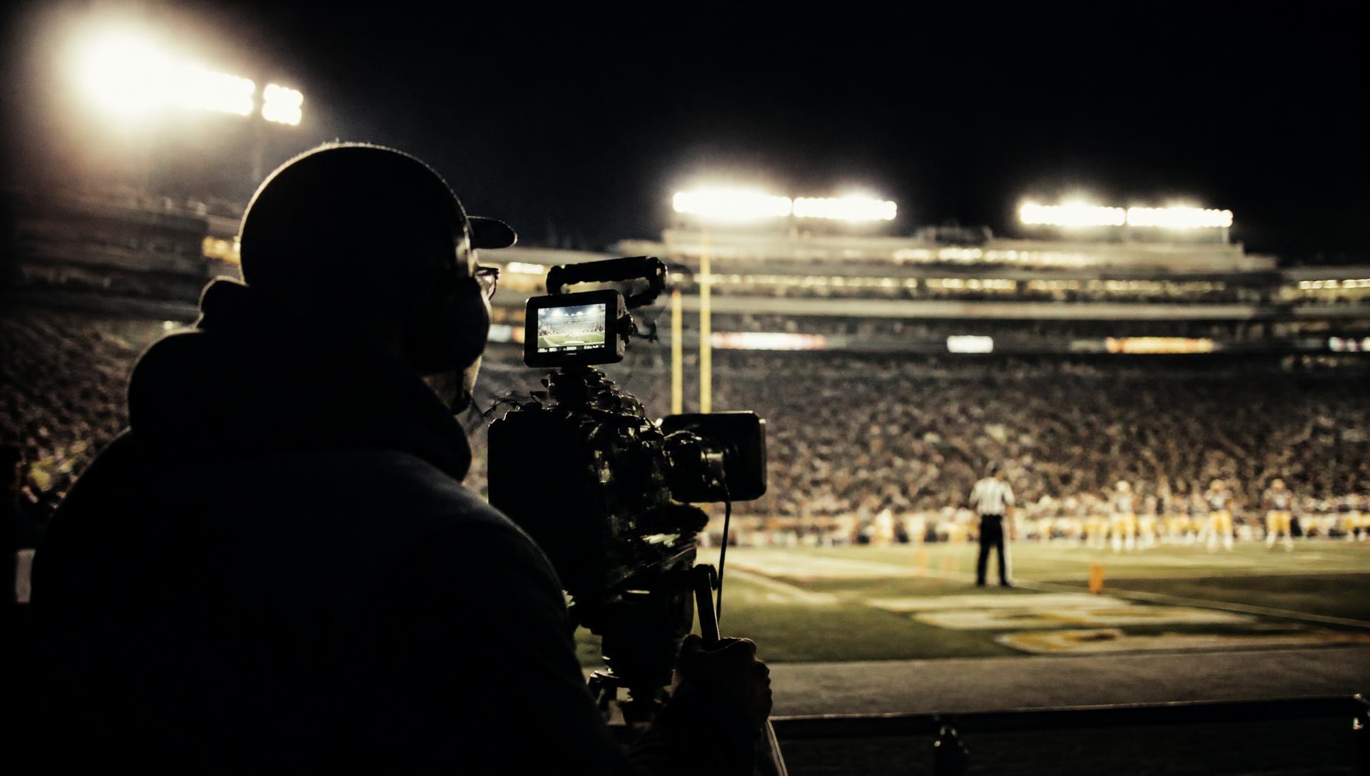 Camera operator filming a floodlit stadium at night